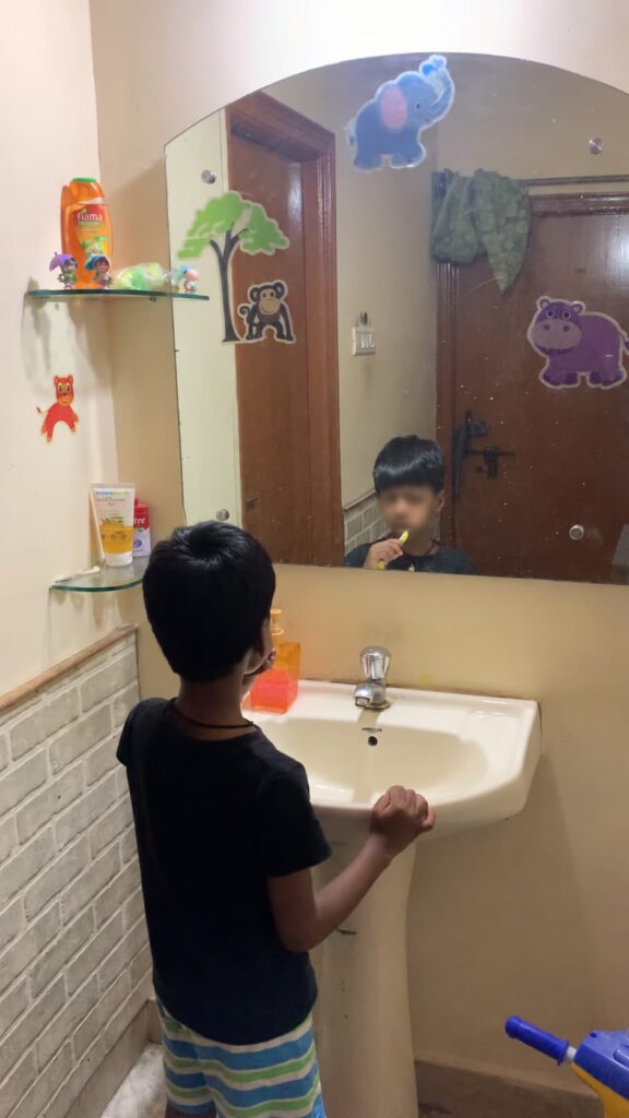 Child brushing his teeth at home as part of a daily self-care routine while looking into a bathroom mirror.