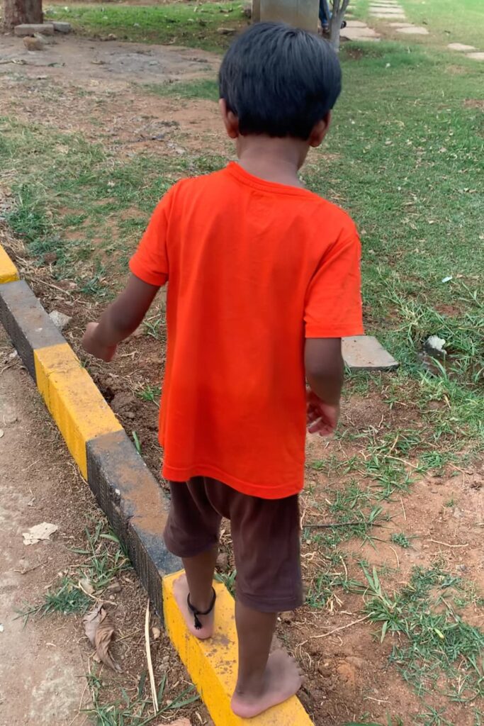 Child practising balance while walking carefully along a curb during an outdoor activity in a park.