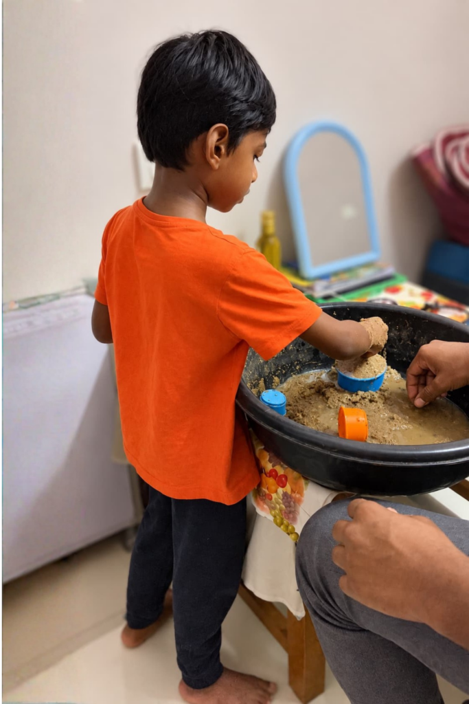 Child exploring sand and water during a hands-on sensory play activity with a caregiver.