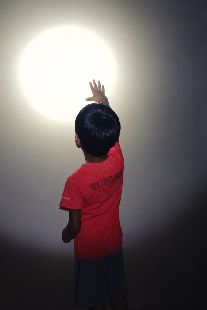 Child reaching towards a light on the wall during an indoor activity, symbolising curiosity, exploration, and growth.