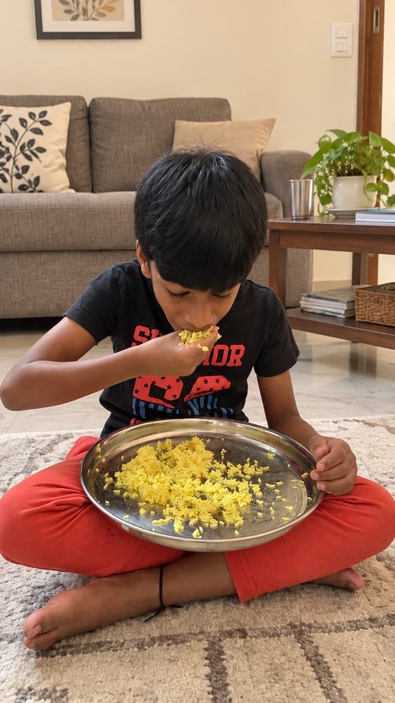 Child eating a meal independently while sitting on the floor at home as part of a daily mealtime routine.